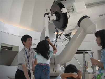 65センチ望遠鏡を使って観察会を行った時の写真。望遠鏡を覗く子どもを職員がサポートしているところ。