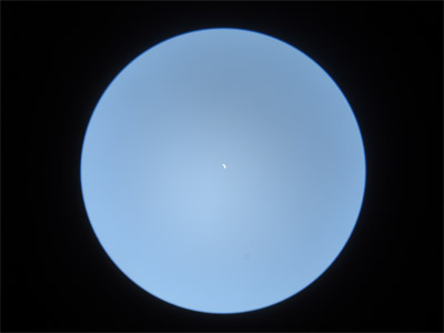 望遠鏡で見た昼間の金星の写真。青空の中に、欠けた形で白く光る金星が見える。